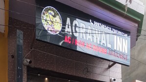 The exterior of the Agrawal Inn, featuring a glass entrance, a brick facade, and a signboard with contact information. - AGRAWAL INN Guest House  (Mathura)