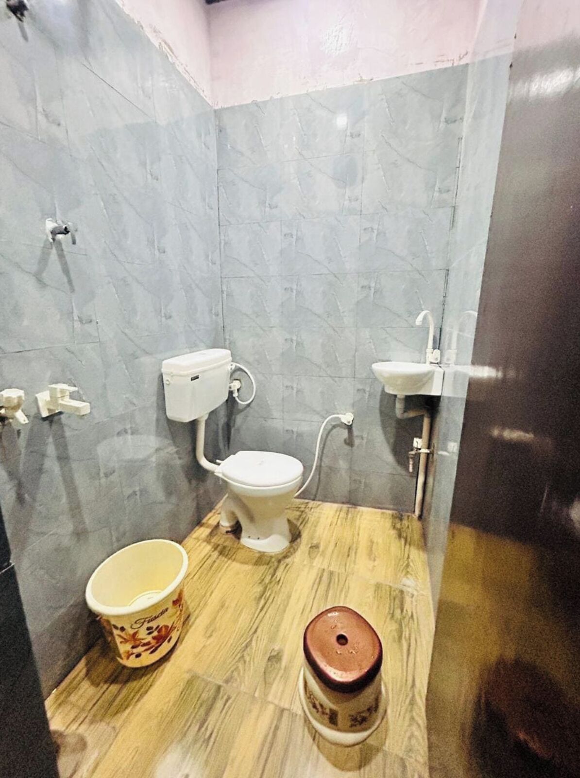 A small bathroom with a toilet, sink, and a bucket on the floor.