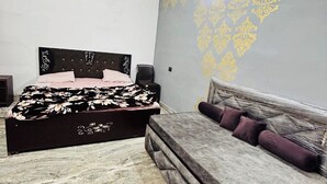 A bedroom with a bed, a sofa, a ceiling fan, and patterned wallpaper. - AGRAWAL INN Guest House  (Mathura)