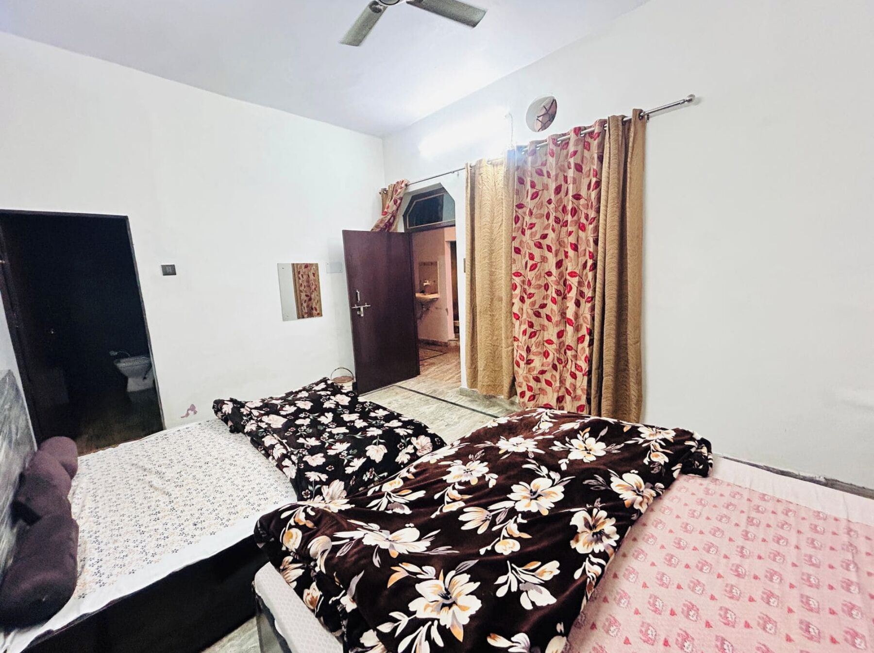 Habitació amb dos llits, un armari, un ventilador al sostre i una finestra amb cortines.