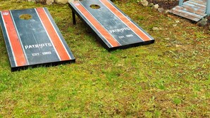 Two wooden boards with "PATRIOTS" and "EST. 1980" text, placed on grass with rocks and a wooden bench nearby. - Lakeside Lagoon W/ Kayaks & Beach Pass (Middleton)