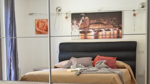 A modern bedroom with a large bed, a cityscape painting on the wall, and a wooden floor. - Villa in Sardinia 5 minutes from the beach (Porto Torres)