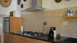 A modern kitchen with a gas stove, wooden cabinets, and a black countertop. - Villa in Sardinia 5 minutes from the beach (Porto Torres)