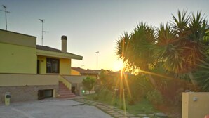 A yellow building with a staircase leading to a door, surrounded by a paved area and palm trees. - Villa in Sardinia 5 minutes from the beach (Porto Torres)