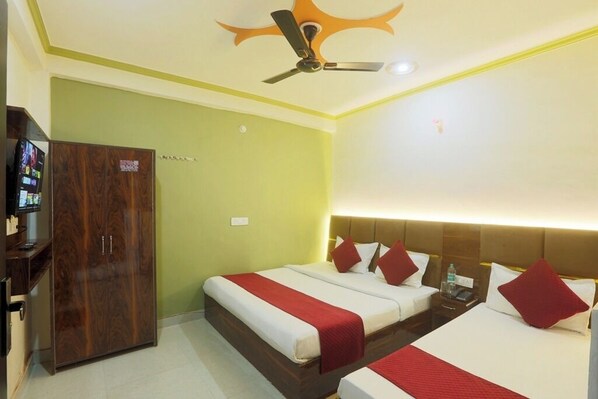 Habitación de hotel con dos camas, un armario, ventilador de techo y televisor sobre un mueble.