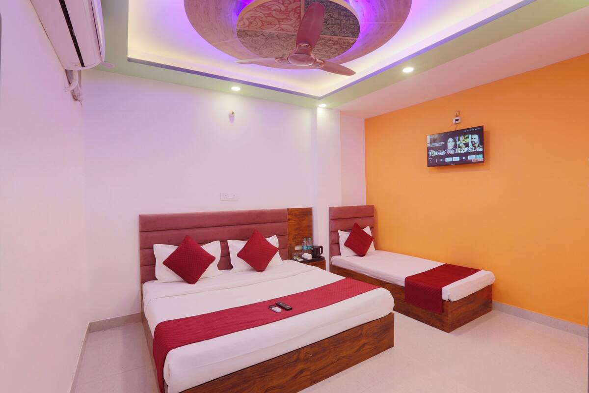 A hotel room with two beds, a ceiling fan, a TV on the wall, and a small table with a bottle and a cup.