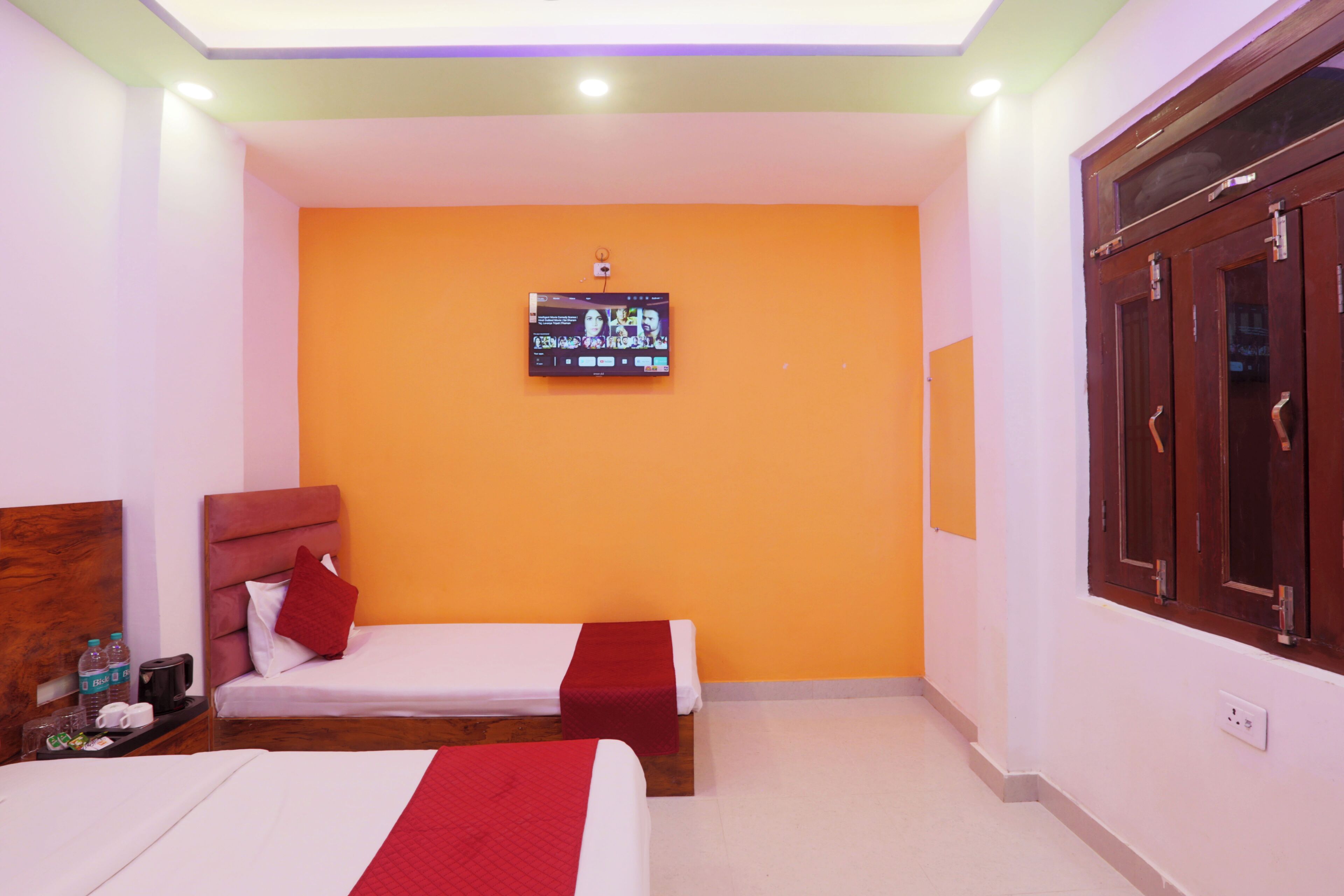 A hotel room with two beds, a television mounted on the wall, and a wooden wardrobe.