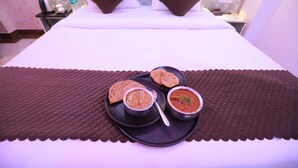 Un lit bien fait, avec des oreillers, une table de chevet sur laquelle se trouve une lampe, et un plateau avec de la nourriture et un bol de soupe.