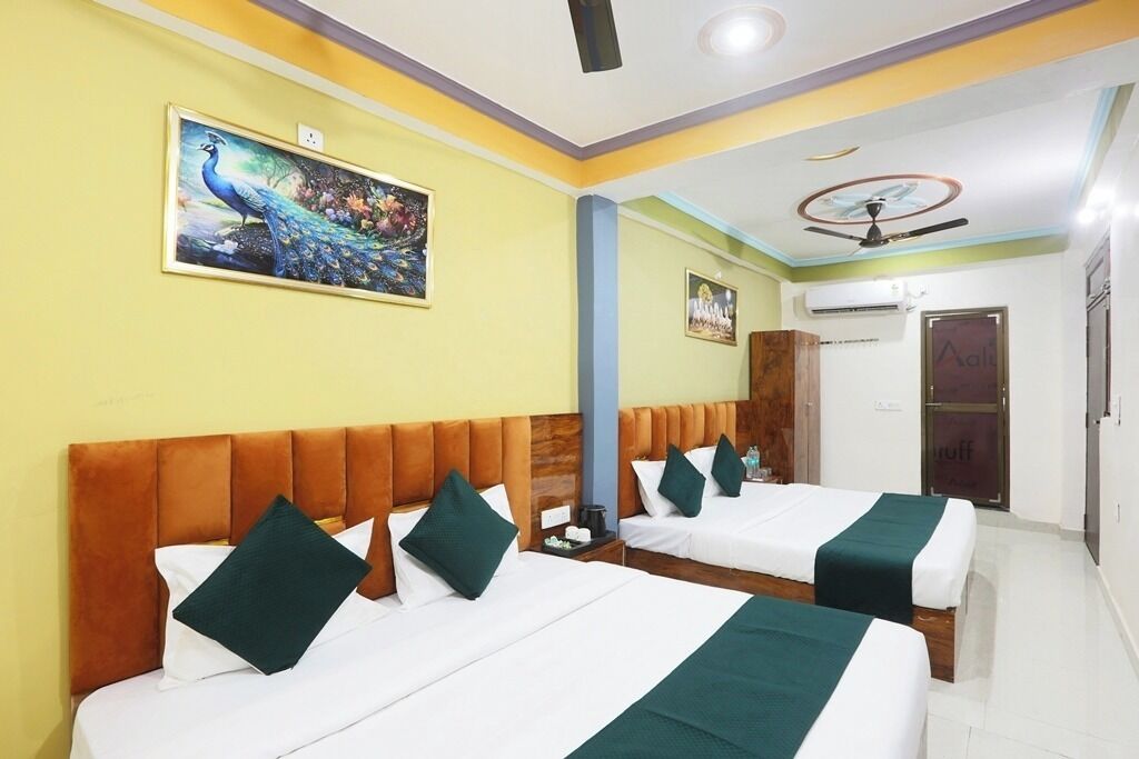 A hotel room with two beds, each with white linens and green pillows, a peacock painting on the wall, and a ceiling fan.