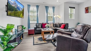 A modern living room with a large flat-screen TV, a sectional sofa, a coffee table, and a decorative plant.