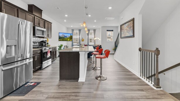 A modern kitchen with stainless steel appliances, a central island with stools, and a staircase leading to another level.