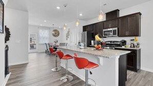 A modern kitchen with dark cabinets, a central island with bar stools, stainless steel appliances, and pendant lighting.