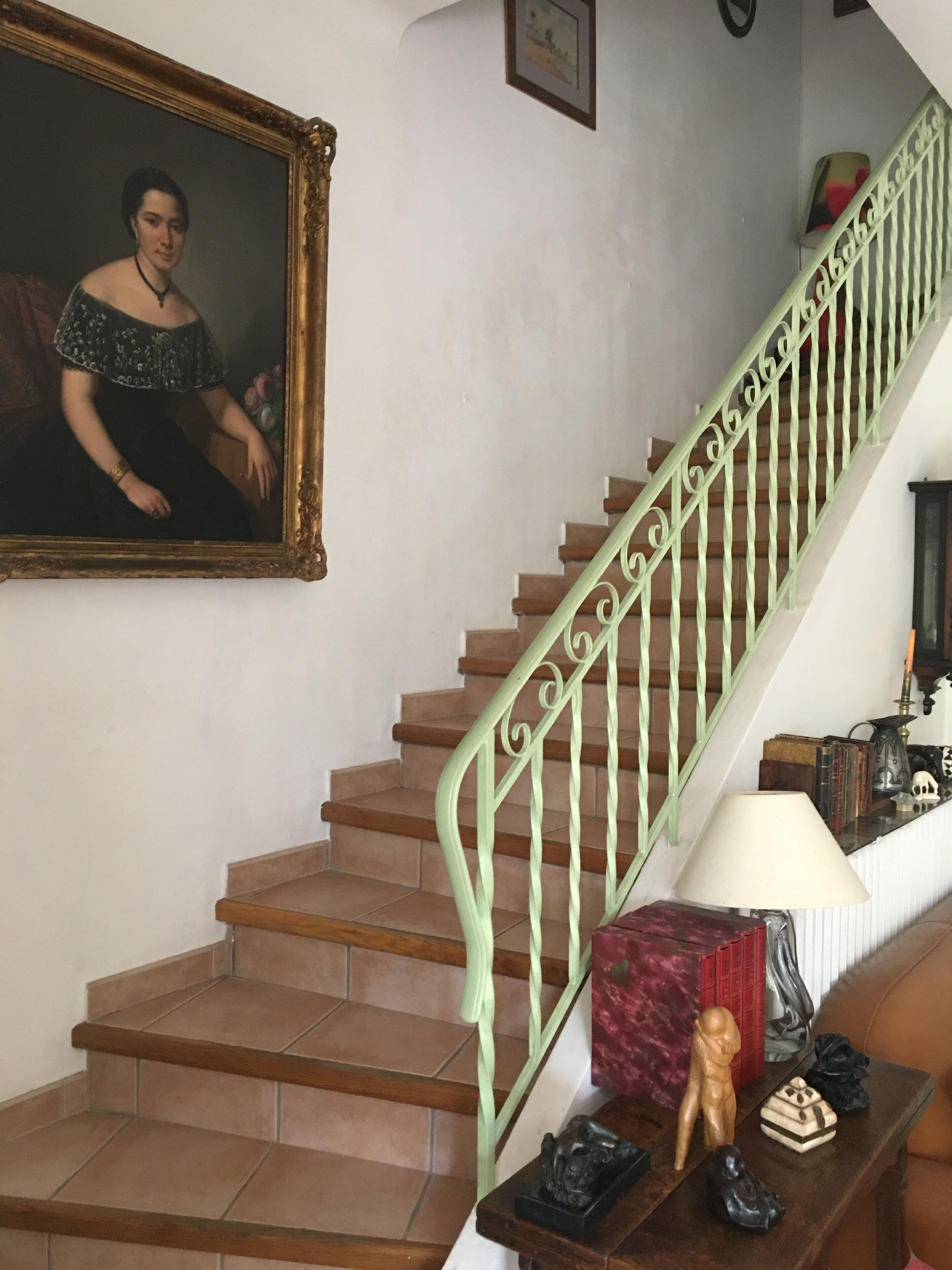 A staircase with green railings, a framed portrait, and a small table with various items.
