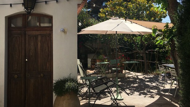 An outdoor patio area with a wooden door, a large umbrella, and several tables and chairs.