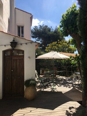 Ein Terrassenbereich im Freien mit einer Holztür, einem großen Sonnenschirm und mehreren Tischen und Stühlen.