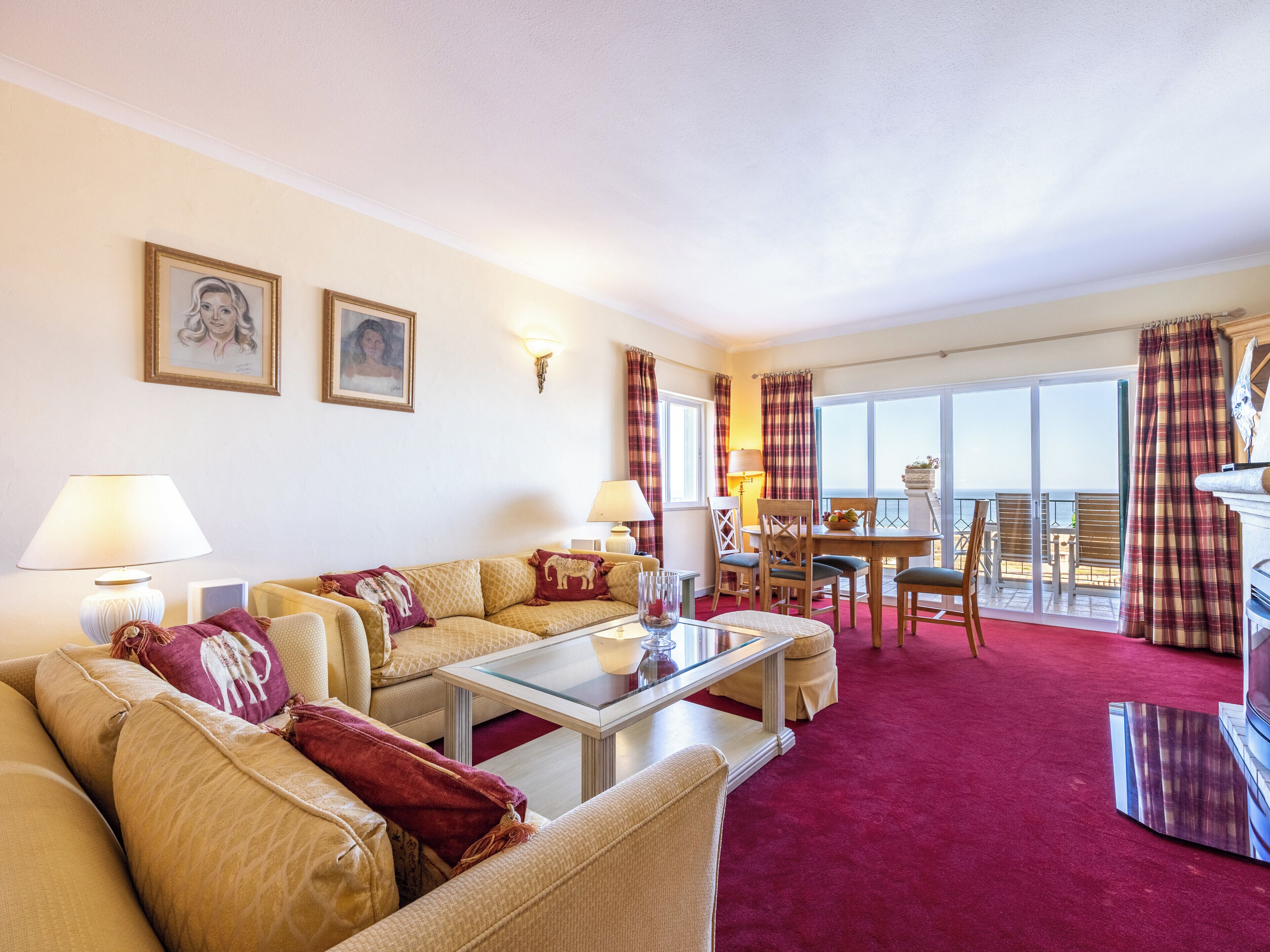 Ein Hotelzimmer mit einer Sofagarnitur, einem Esstisch mit Stühlen, einem Balkon mit Blick und zwei Wandleuchten.