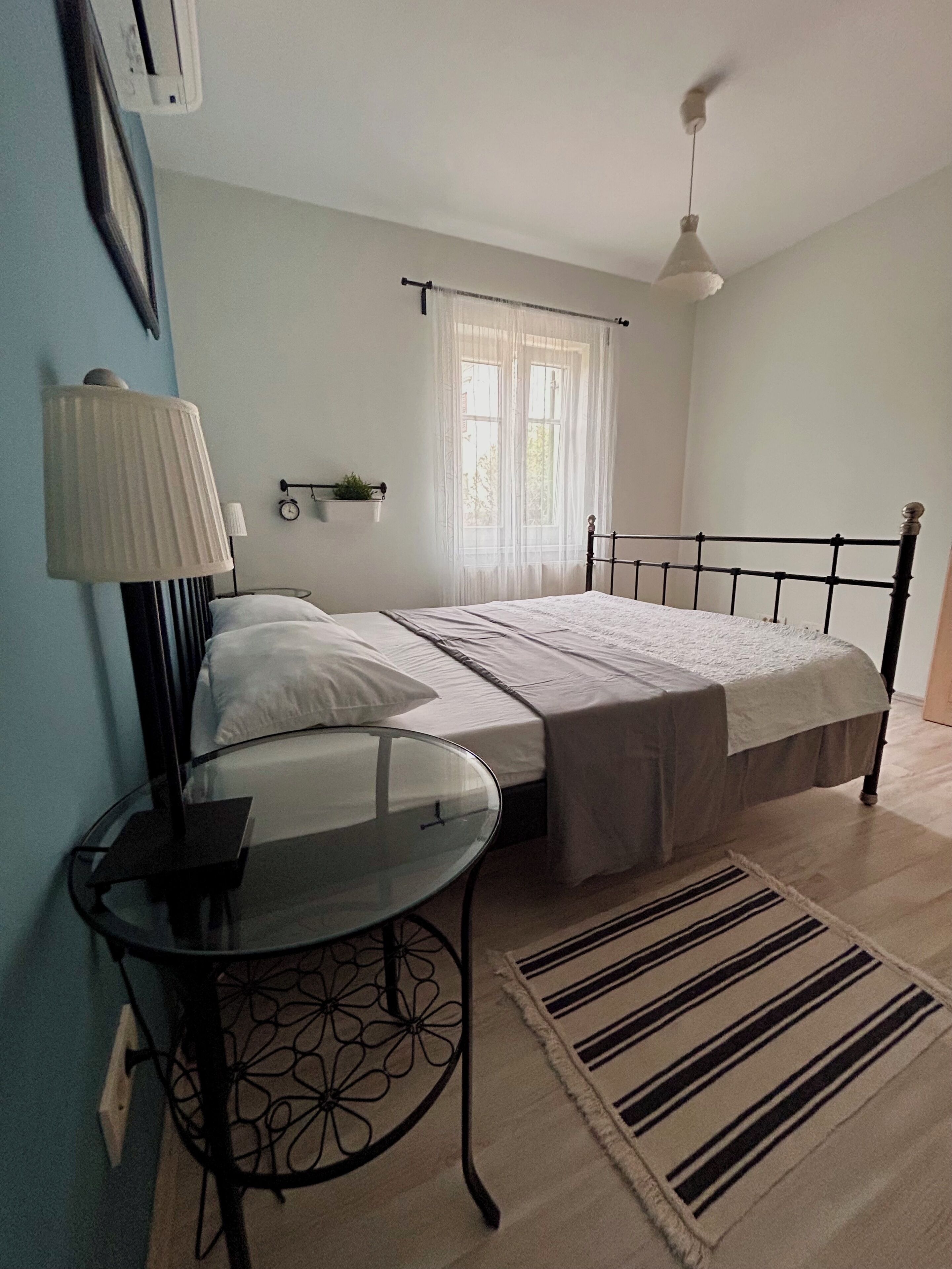 A bedroom with a bed, bedside table, lamp, window, and a hanging light fixture.