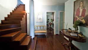 A wooden staircase leading to a landing, a bench, a table with a vase and books, and a framed portrait on the wall.