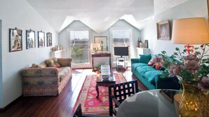 A cozy living room with a patterned sofa, a teal couch, and a coffee table. There are framed pictures on the wall and a lamp on a side table.