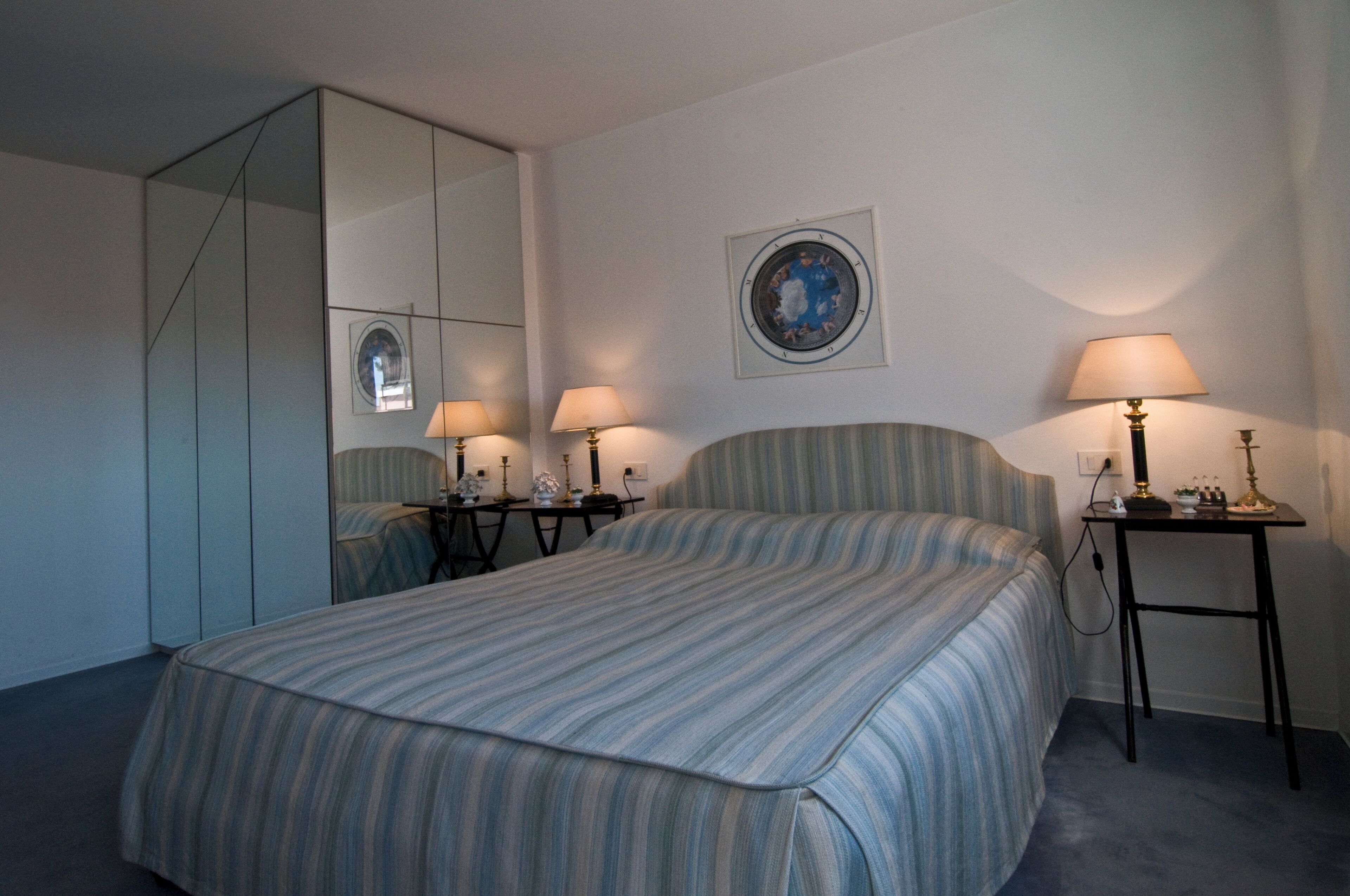 Quarto com uma cama grande, duas mesas de cabeceira com abajures, um espelho e um relógio na parede.