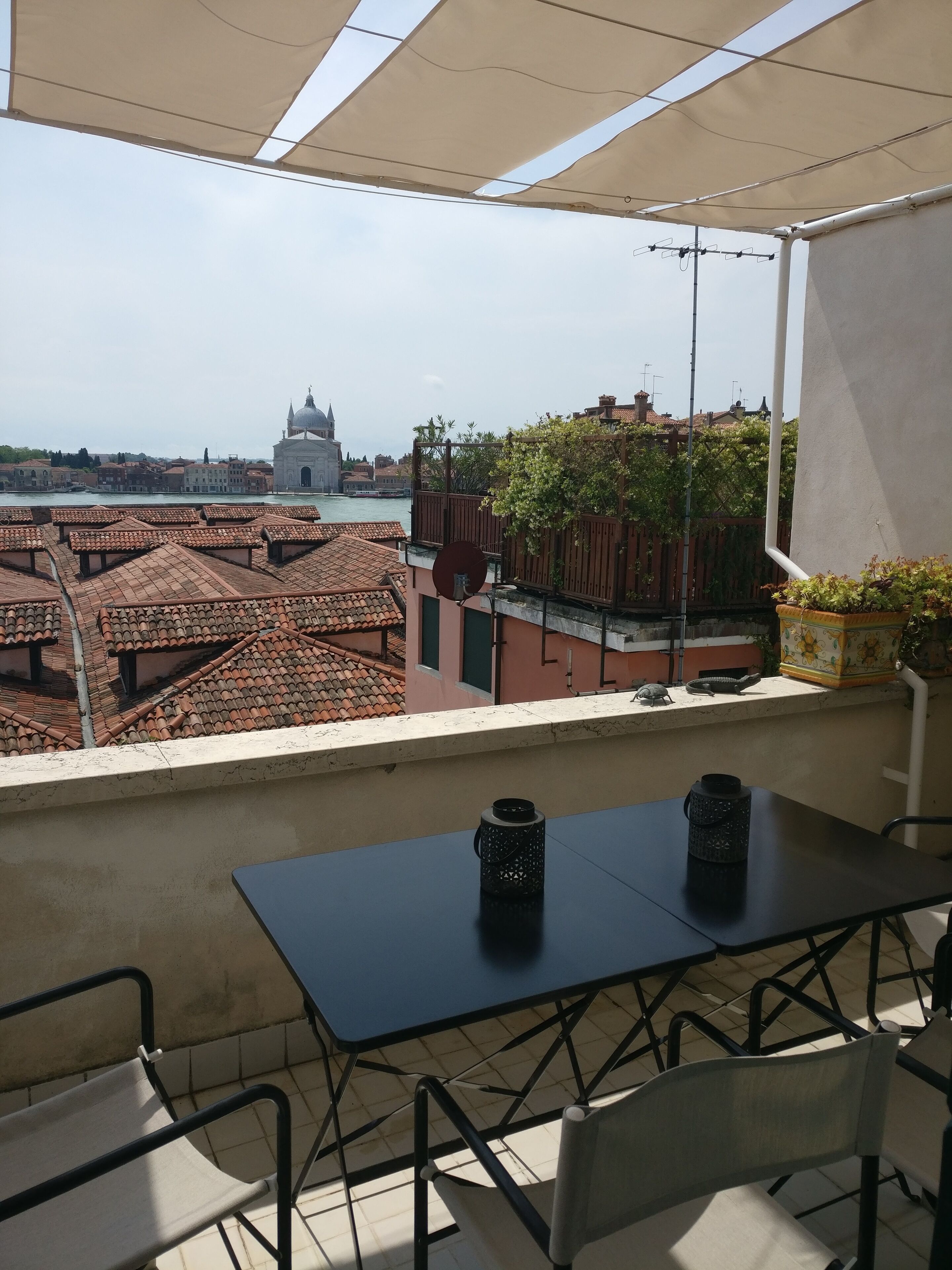 A terrace with a table and chairs, overlooking a cityscape with terracotta rooftops and a historic building.