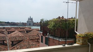 A terrace with a table and chairs, overlooking a cityscape with terracotta rooftops and a historic building.