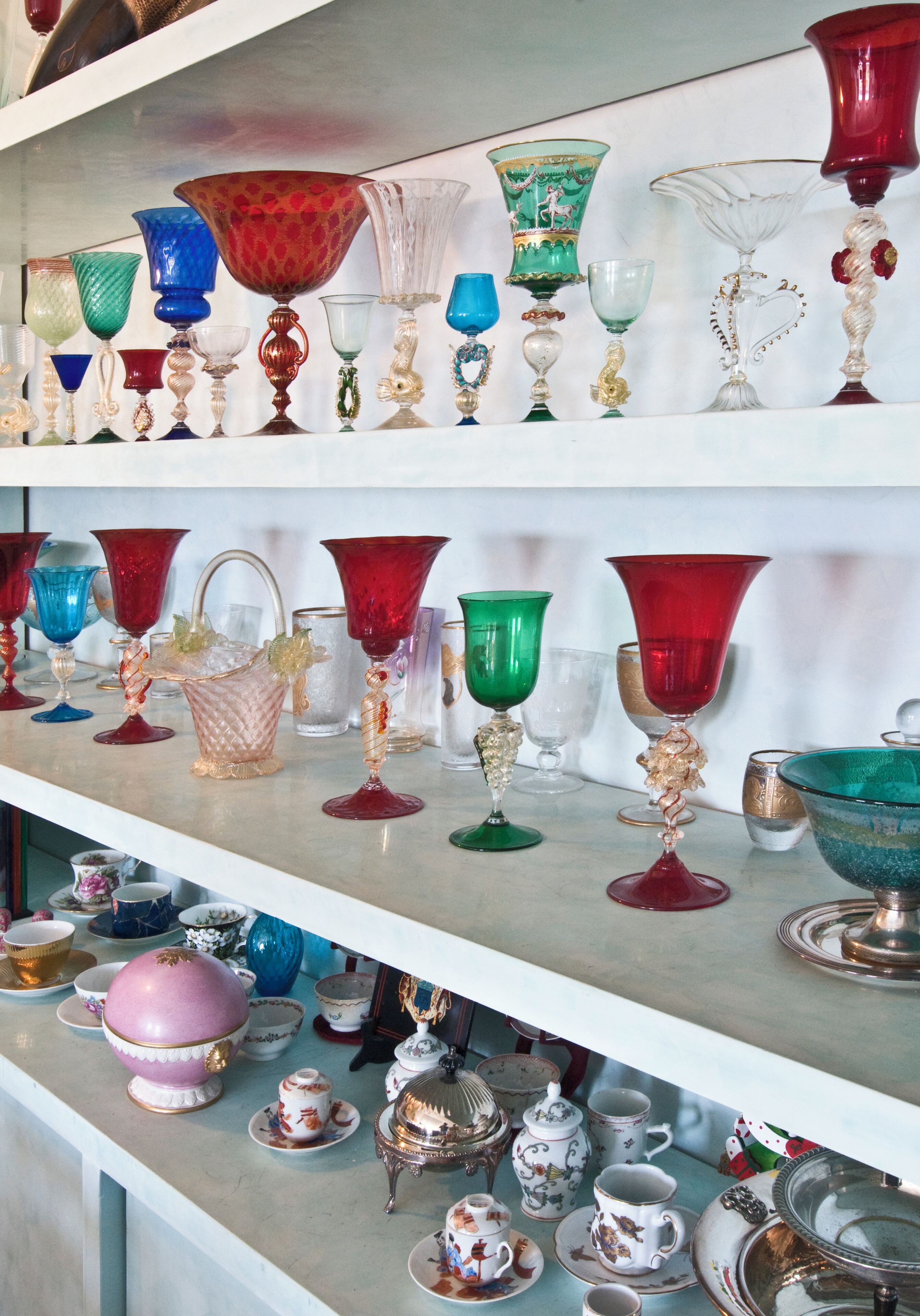 Una exhibición de diferentes objetos de vidrio y porcelana en estantes.