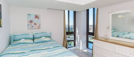 Ein Schlafzimmer mit einem Bett, einem Schminktisch, einem Bild und einem großen Fenster.