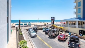 Een parkeerplaats met auto's, uitzicht op het strand en een gebouw met een balkon.