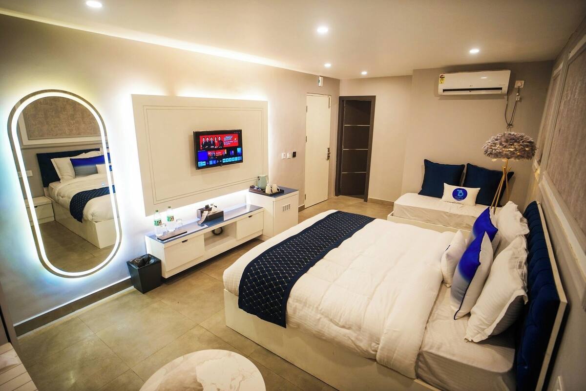 A modern hotel room with a large bed, a bedside table, a TV mounted on the wall, and an air conditioning unit.