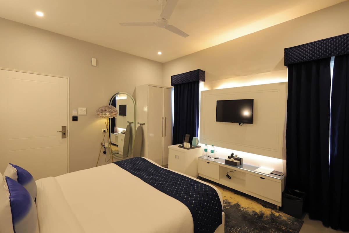 A hotel room with a bed, a vanity with a mirror, a television, and a desk with a lamp.