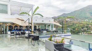 Terraza en la azotea con mobiliario exterior, barandilla de cristal y vistas a un lago y colinas.