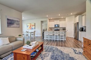 A modern kitchen with white cabinets, a central island with bar stools, and a dining area with a table and chairs.
