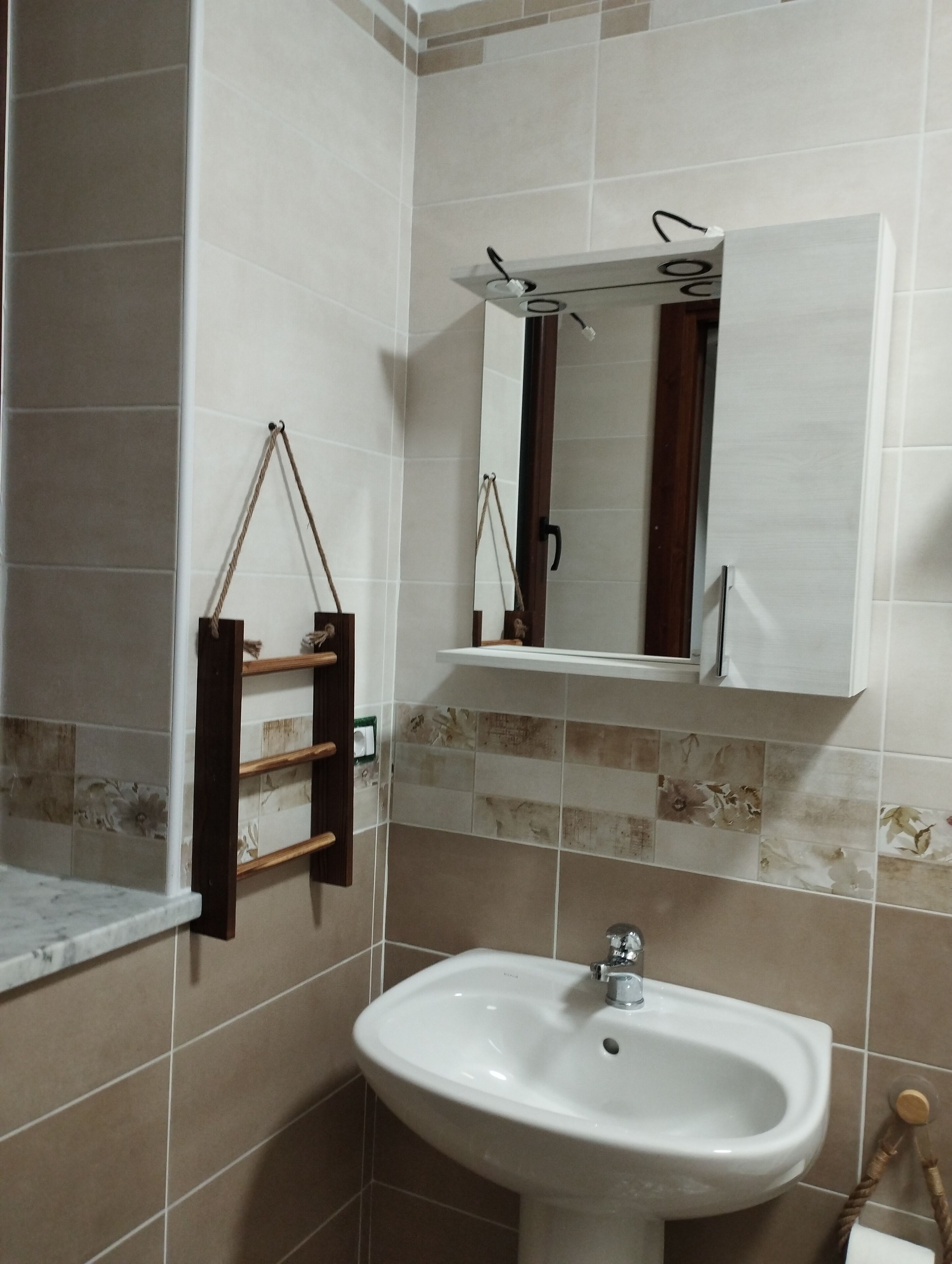 Ein Badezimmer mit Waschbecken, Spiegel, Handtuchhalter und gefliesten Wänden.