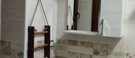 Ein Badezimmer mit Waschbecken, Spiegel, Handtuchhalter und gefliesten Wänden.