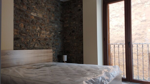 A bedroom with a stone wall, a bed with a wooden headboard, a nightstand, and a view of a balcony. - Corleone bed and breakfast  (Corleone)