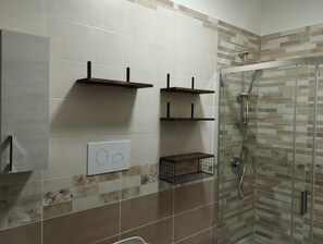 A bathroom with a glass shower enclosure, a towel rack, and a shelf unit. - Corleone bed and breakfast  (Corleone)