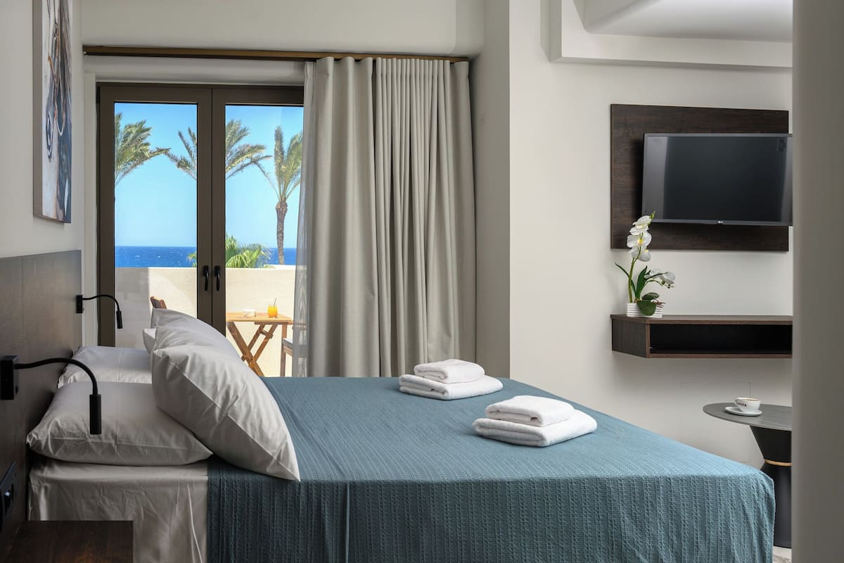 Habitación de hotel con cama, televisión montada en la pared y vista al océano a través de la ventana.