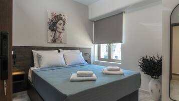 A modern bedroom with a large bed, a bedside table, a wall-mounted TV, a window with a blind, and a decorative vase.