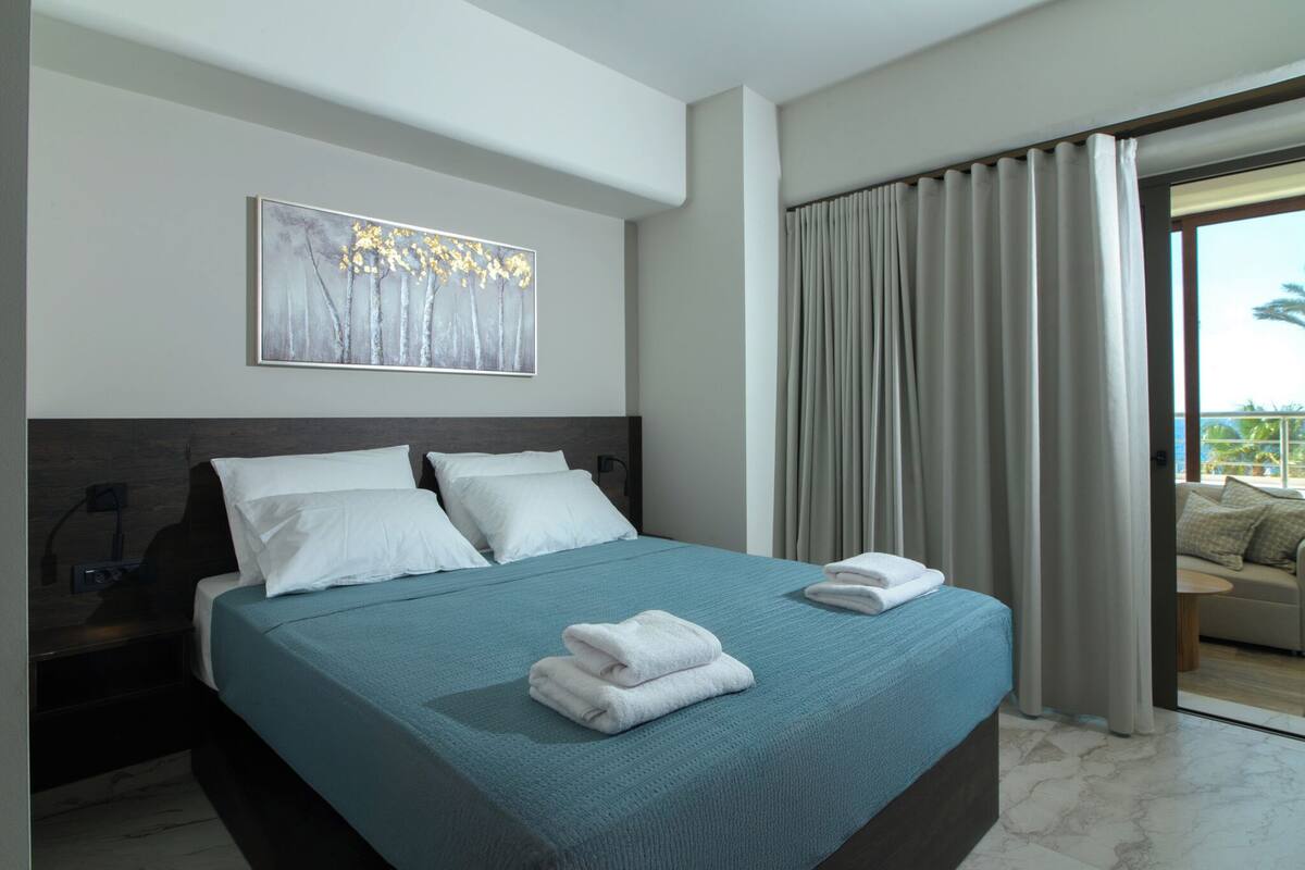 Una habitación de hotel moderna con una cama grande, un cuadro en la pared y vistas al exterior a través de una puerta corredera.