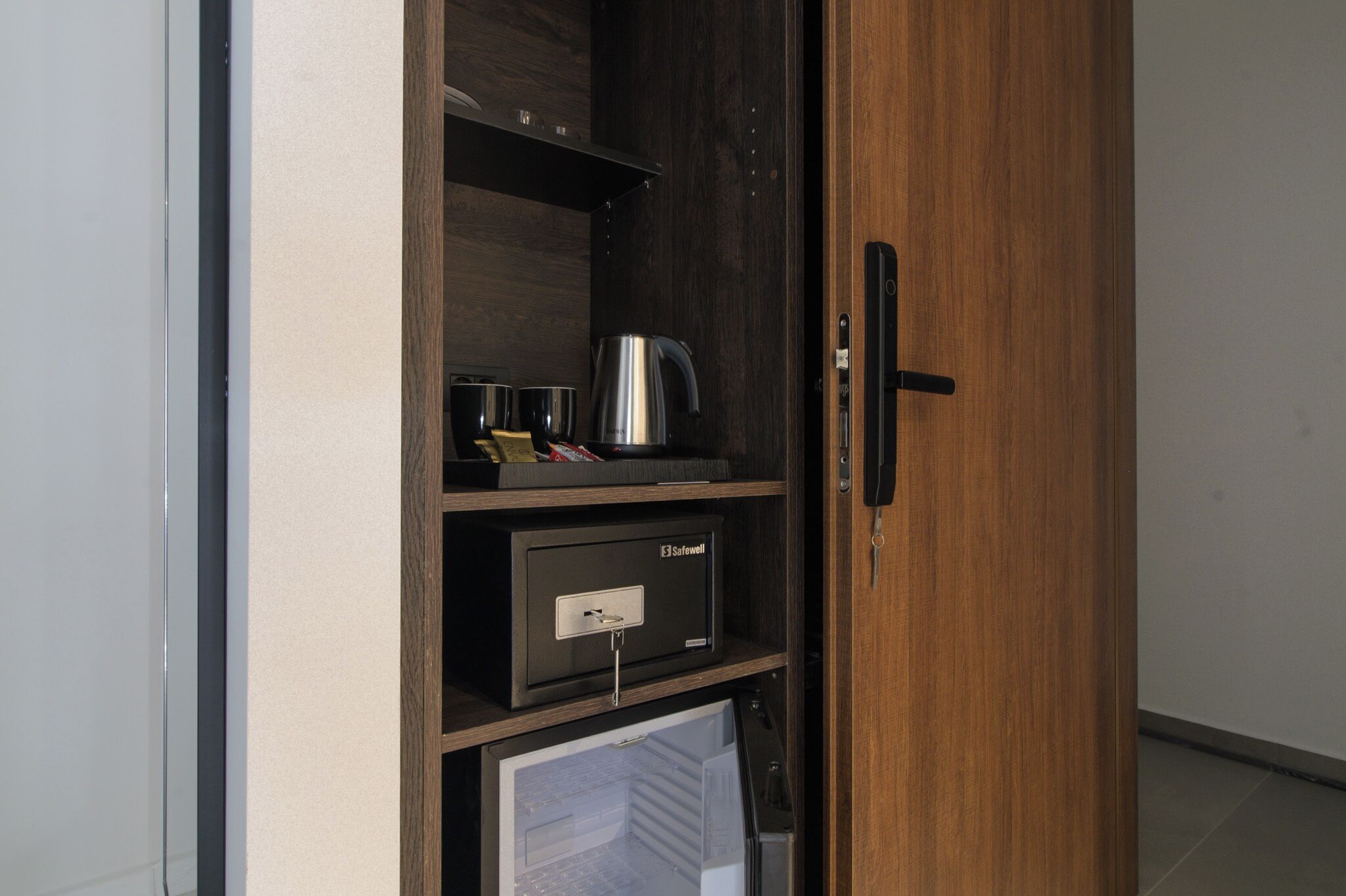 A wooden cabinet with a safe, a kettle, and a refrigerator.