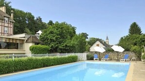 A swimming pool with lounge chairs and umbrellas, surrounded by greenery and traditional buildings. - Domaine des Chateaux (Chaumont-sur-Loire)