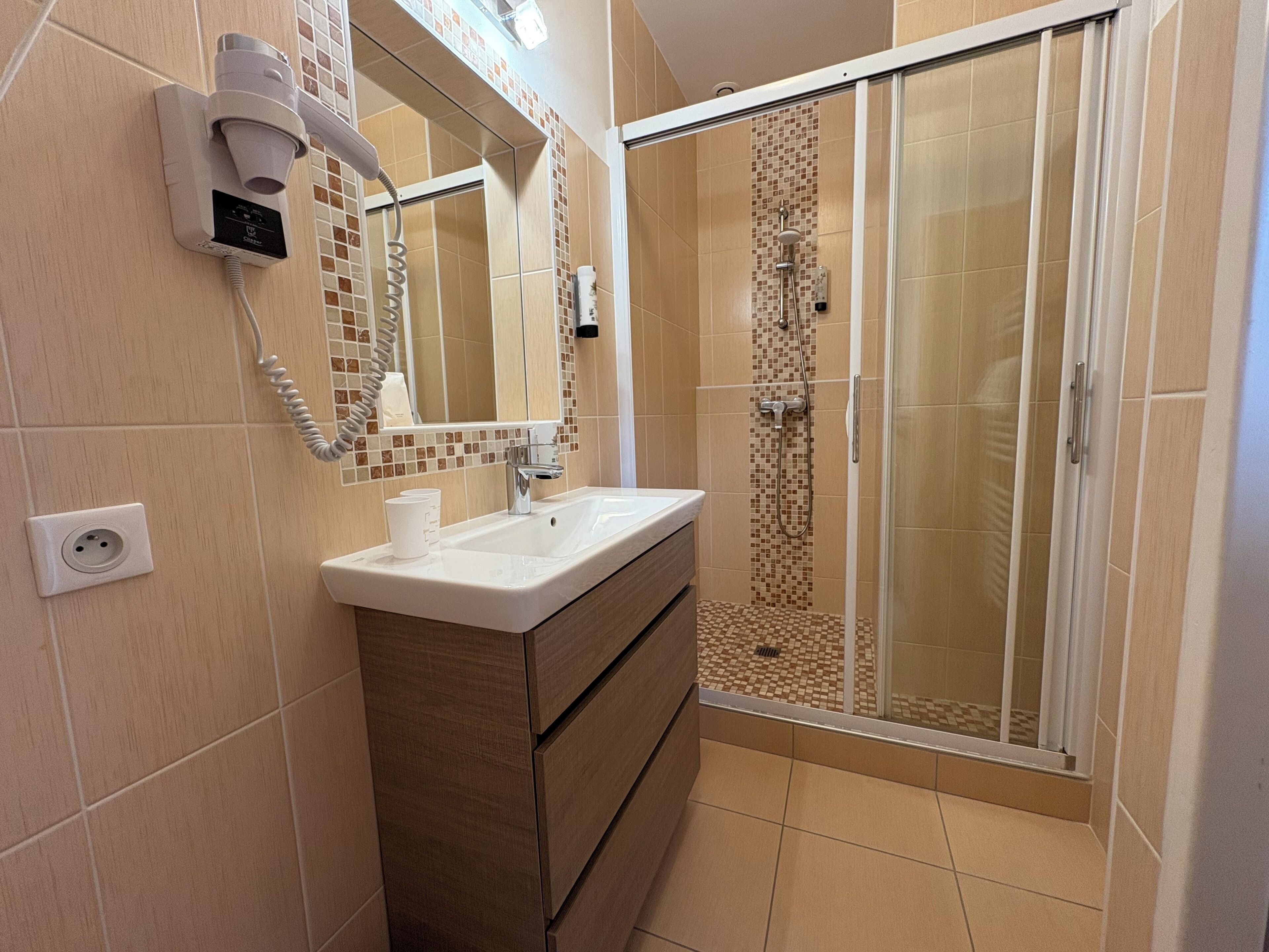 A modern bathroom with a shower, a vanity with a mirror, and a hairdryer mounted on the wall.