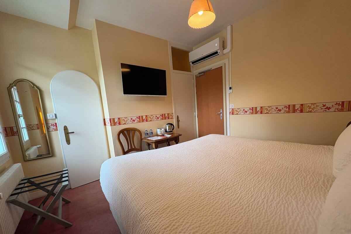 Habitación de hotel con cama, escritorio, silla, espejo, equipo de aire acondicionado y puerta.