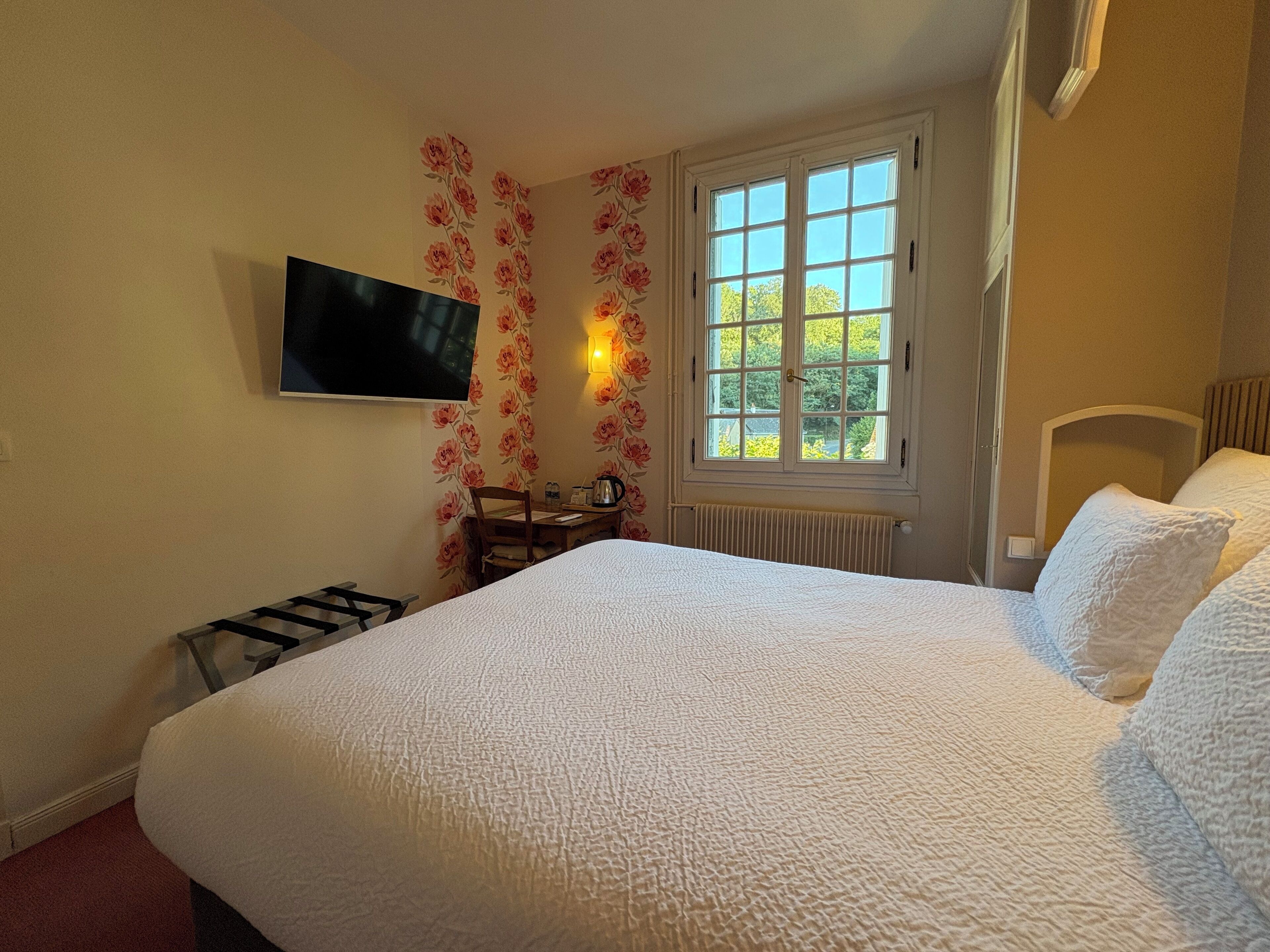 Ein Schlafzimmer mit einem großen Bett, einem flachbildfernseher an der Wand, einem Fenster mit Blick ins Grüne und einer Heizung.