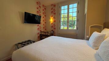 Ein Schlafzimmer mit einem großen Bett, einem flachbildfernseher an der Wand, einem Fenster mit Blick ins Grüne und einer Heizung.