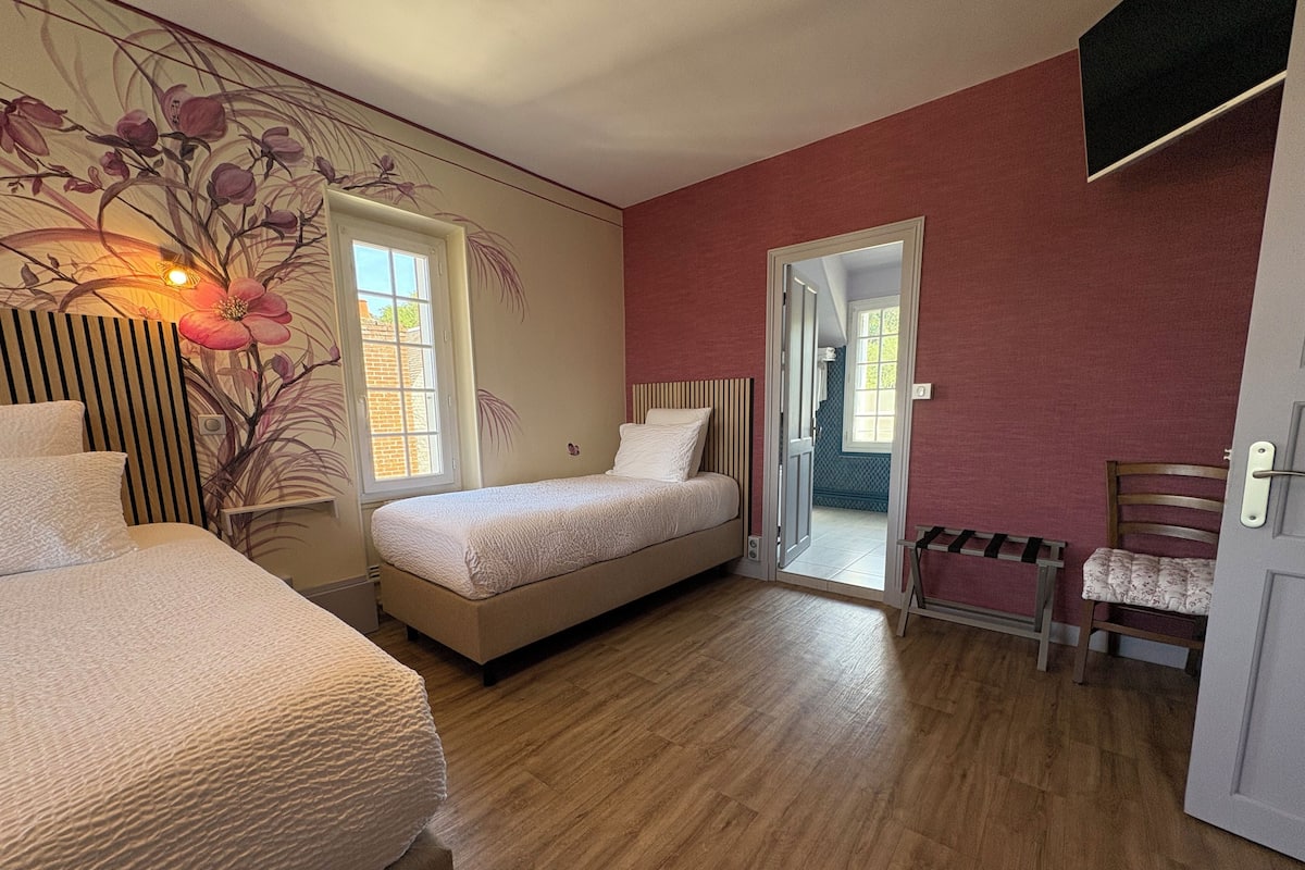 Un dormitorio con dos camas, suelo de madera, una puerta que da a un balcón y una silla.
