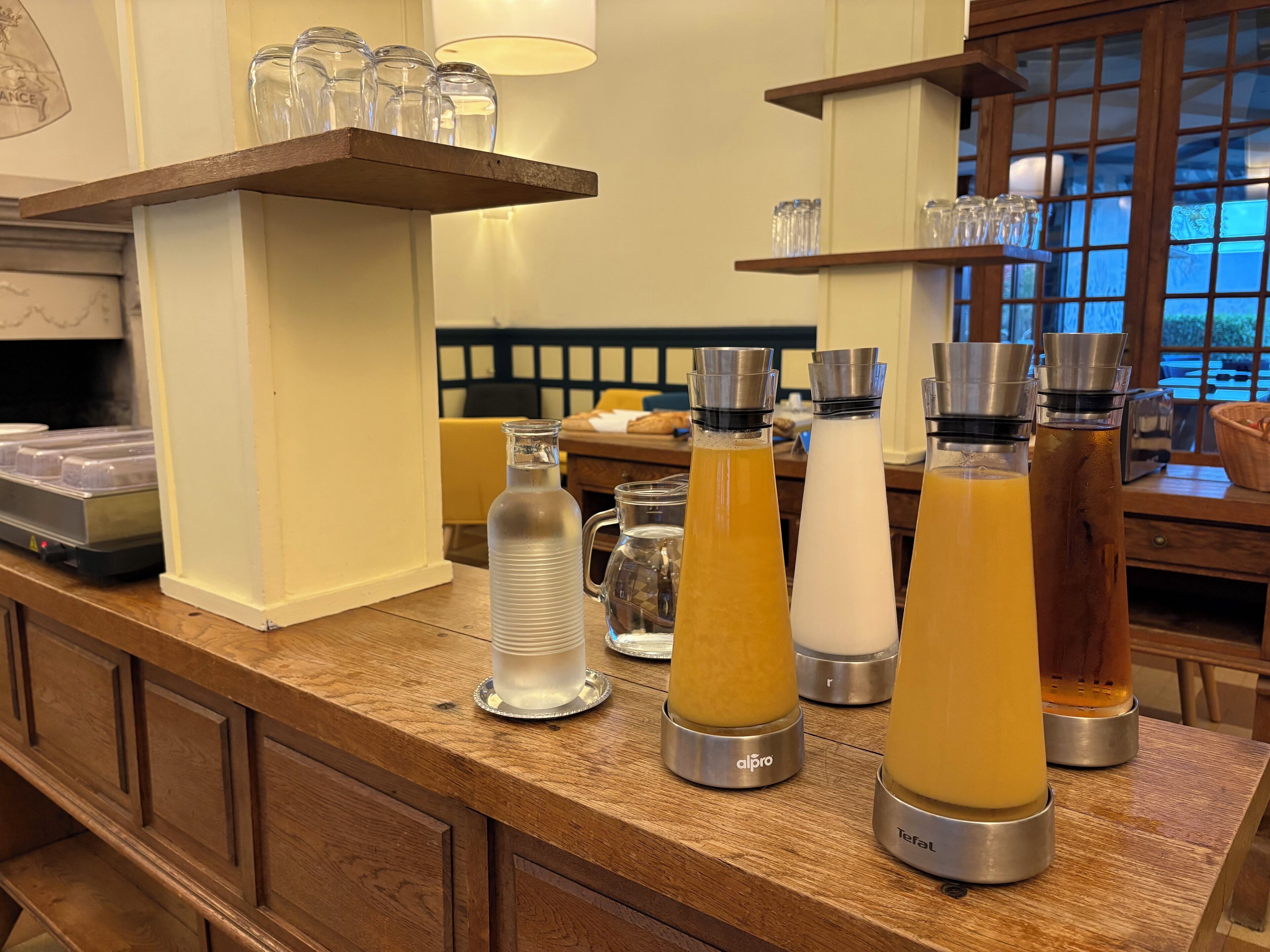 A bar area with various beverage dispensers and a shelf with glasses.