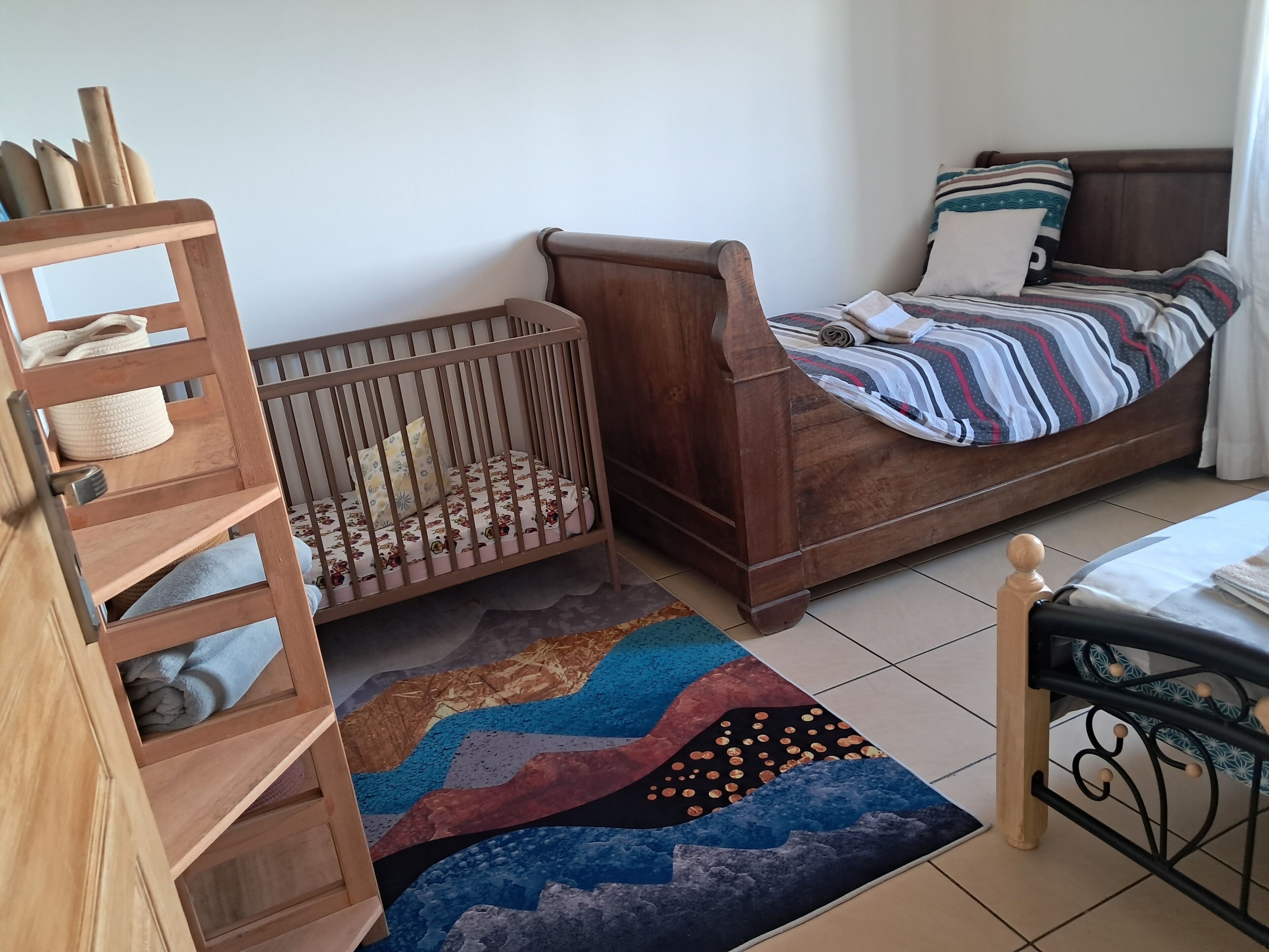 Una stanza con una culla, un letto, un mobiletto a mensole in legno e un tappeto colorato.