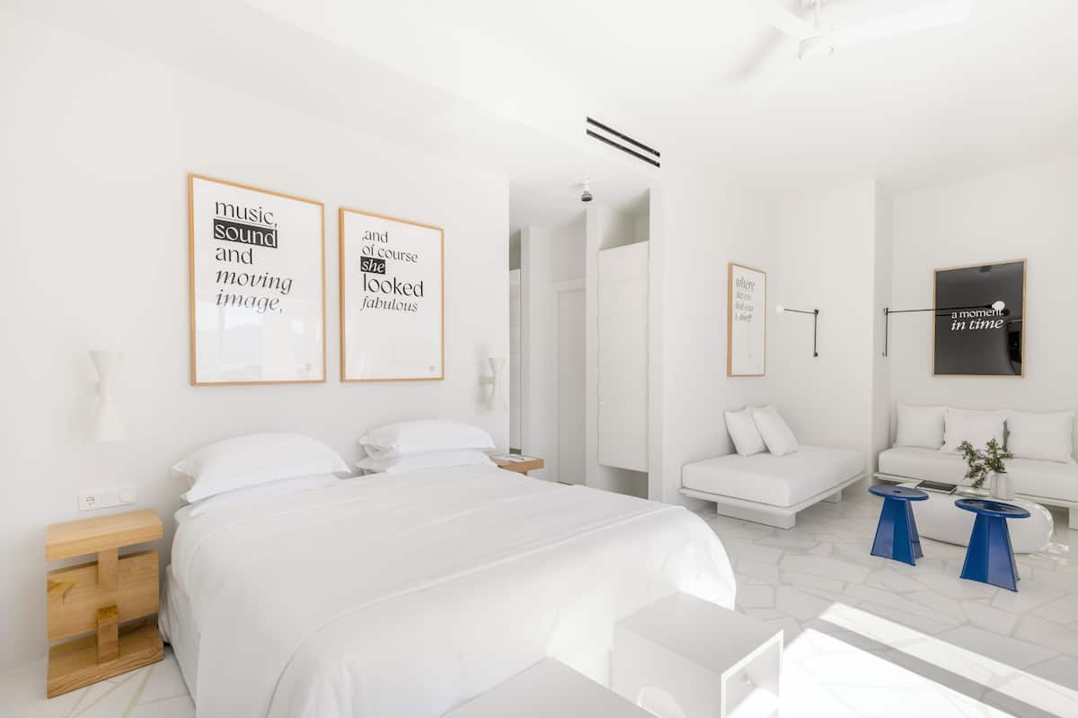 Una habitación de hotel moderna con una cama grande, un sofá, una mesita de café y cuadros en las paredes.